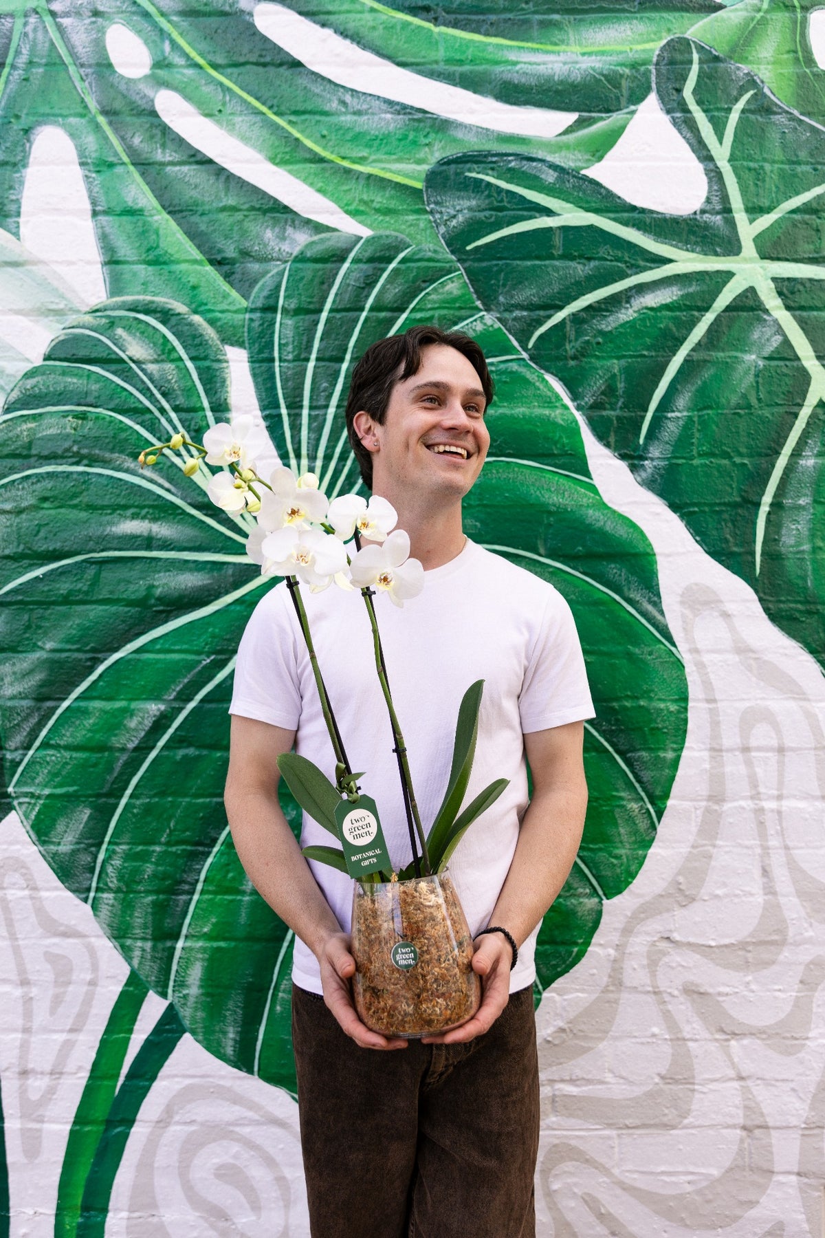 Jake Simmons holding an orchid in front of the Two Green Men botanical mural